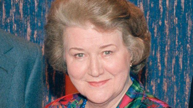 Dame Patricia Routledge, smiling at the camera, wearing a colourful blouse