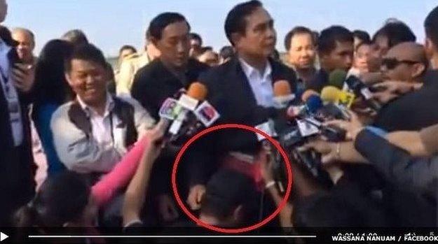 Prime Minister Prayuth Chan-Ocha's hand pats the head of a journalist kneeled in front of him throughout a press briefing