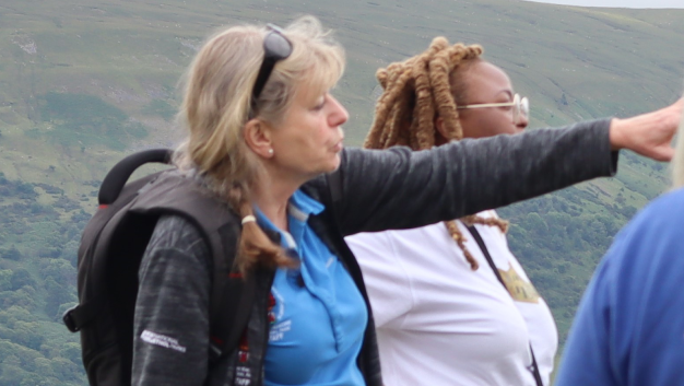 Francesca Bell wearing a team t shirt and a backpack, standing amid a crowd of colleagues in the national park with green landscape behind her