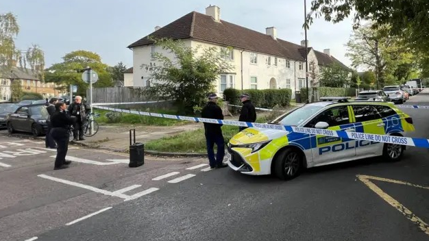 A police car and police officers standing around a police tape as it blocks off a street in north London