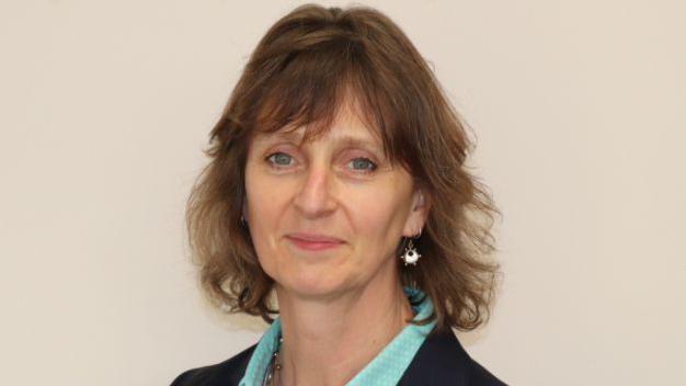 Becky Shaw, wearing a turquoise blouse and a blue jacket, stares into the camera.