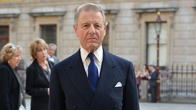 Actor Edward Fox OBE faces the camera in a street. He has combed, light grey hair and wears a dark blue suit with a white pocket square.