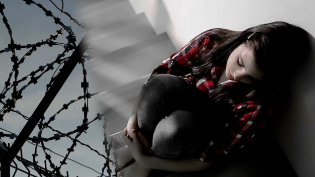 A stock photo of a girl in a stairwell crunched up in the foetal position 