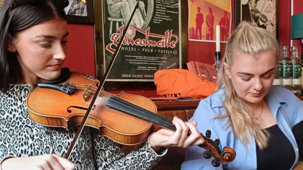 Two women playing music, one on violin and the other on bagpipes