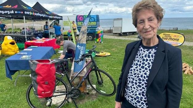 Dame Norma Redfern standing in front of a bike