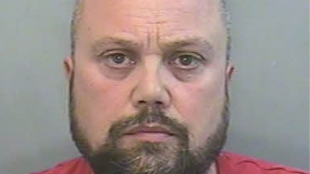 A police mugshot of Craig Short who has a brown beard and is wearing a red top