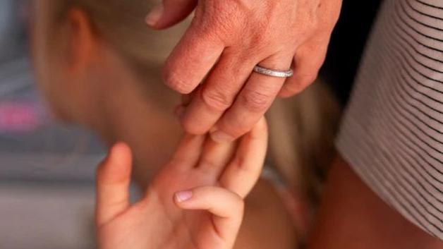 A adult woman's hand holding a young blonde girl's hand