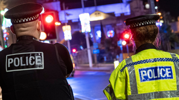 Two police officers facing away from camera in front of street at night