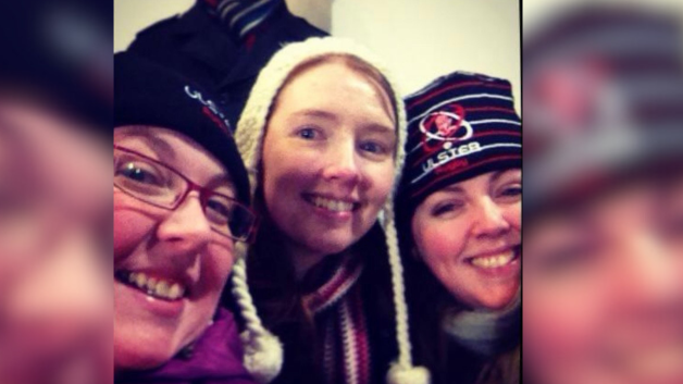 The three sisters pictured up close together. Clare is in the middle wearing a white hat and coloured scarf. Her sisters on either side are wearing black hats.