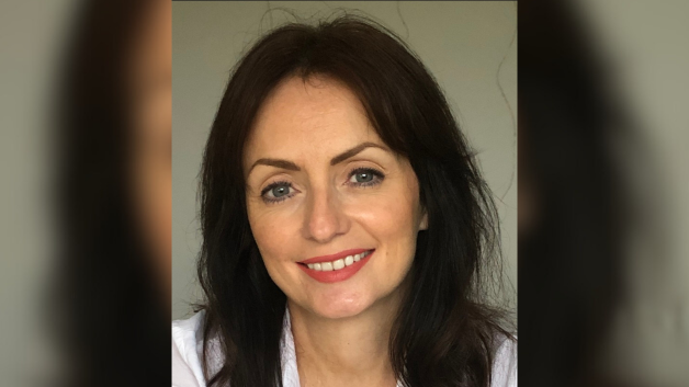 Frances has long dark hair and is smiling at the camera. She is wearing makeup with a pink lipstick, and is wearing a white shirt.