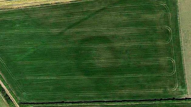 Google Earth overhead photo of a large dark circle embedded in flat green farm with tractor trails visible over it.