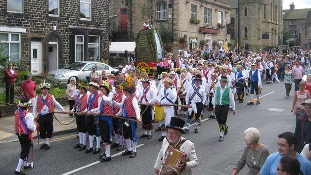 Morris men prepare to pull the rushcart, a tall pyramid of rushes woven together, along the High Street in Uppermill