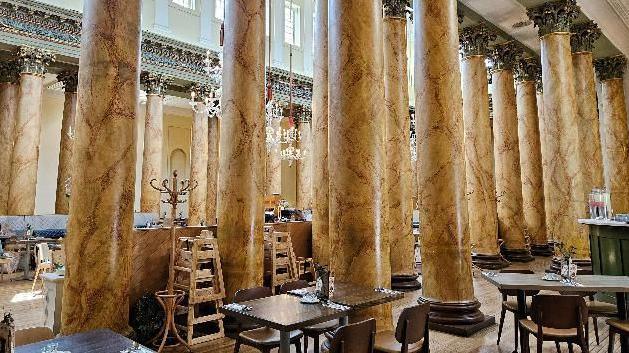 The inside of York's Assembly Rooms. Tables and chairs on a tiled floor next to numerous marble pillars.