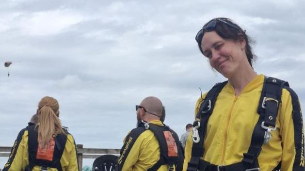 Belinda Taylor pictured wearing a bright yellow jumpsuit with black straps around her