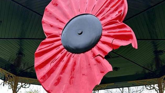 A large red plastic poppy in Eastleigh bandstand, the bottom section of the poppy petal is snapped and cracked in fragments.