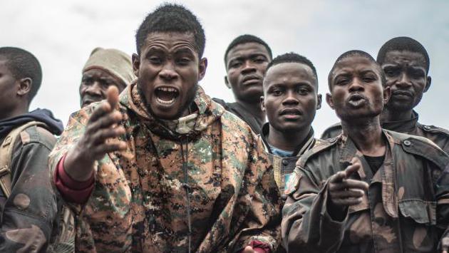 Detained Congolese soldiers shout from a truck after they have been captured. One soldier is raising his army towards the camera.