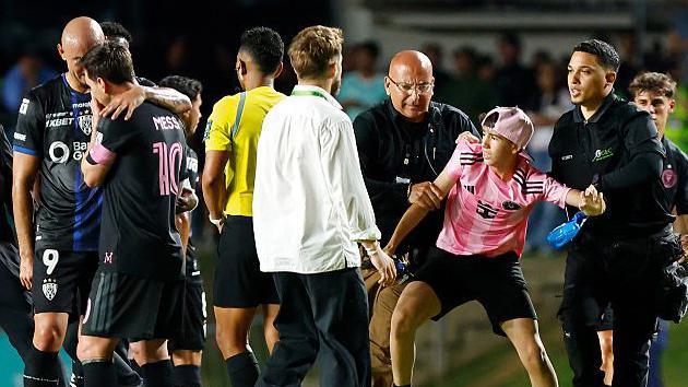 Lionel Messi being led away from another pitch invader