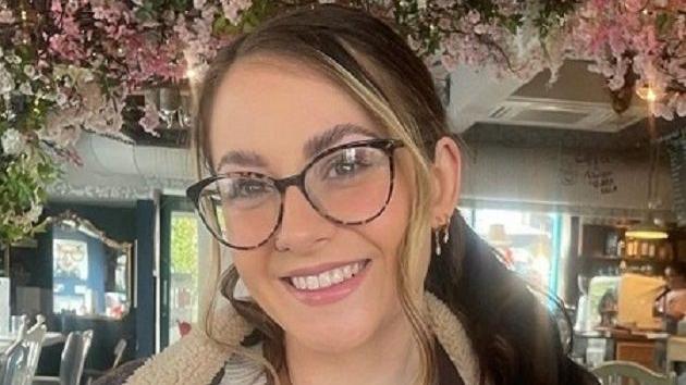 Woman with brown hair and glasses smiles into the camera