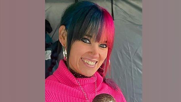 Tiffany Wells is smiling at the camera. She has a pink jumper on - and her hair is coloured dark blue and pink/red.