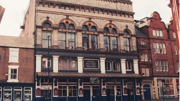 The outside of the Tyne Theatre, a typically Victorian playhouse building on three floors with the biggest windows at the top and pillars on the second floor, There is a sign reading Stoll Picture Theatre 