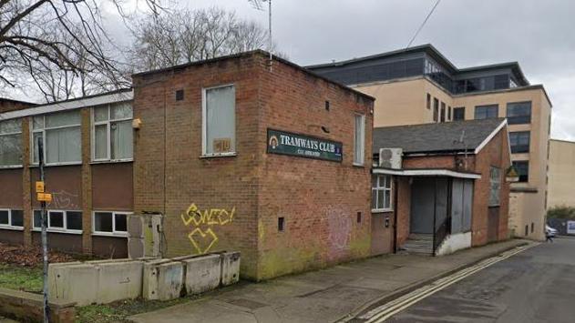 A run-down working men's club, with a boarded-up entrance and graffiti on the walls.