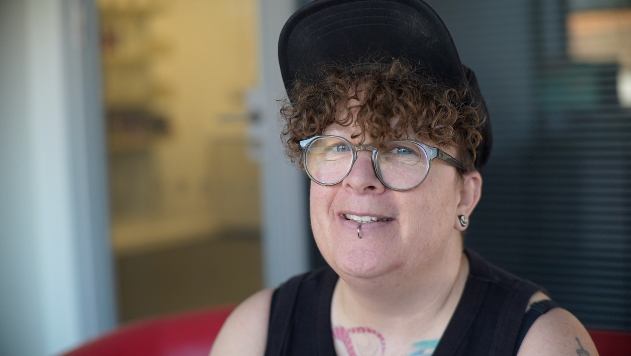 Emma Hastings looks at the camera. She has brown curly hair, wears a cap and glasses and has a lip piercing.