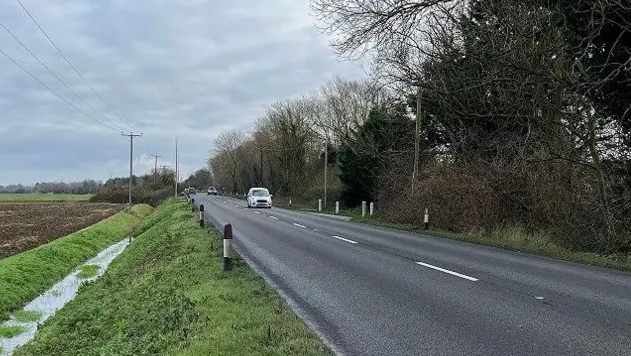 A picture of the A47 near King's Lynn. The two-lane road is next to a ditch with icy water at the bottom. On the right hand side, the rod is flanked by trees. The road is almost empty, but there is one car travelling towards the camera. Two other cars can be seen in the distance.