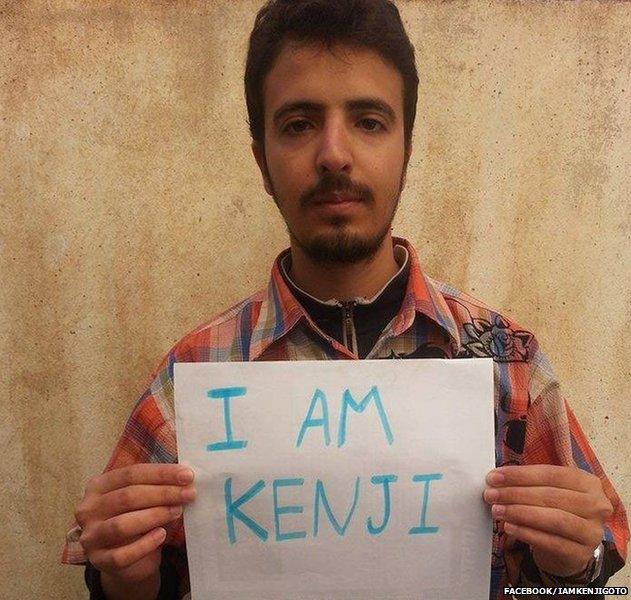 Photo of a man holding a placard that says 'I am Kenji'