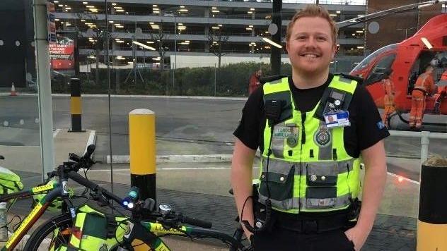 Rob Weldon smiles at camera whilst in paramedic uniform, next to his bike