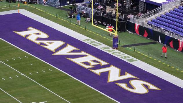 A NFL end zone showing the Ravens text logo and the slogan 'End Racism' stencilled on the edge of the field.