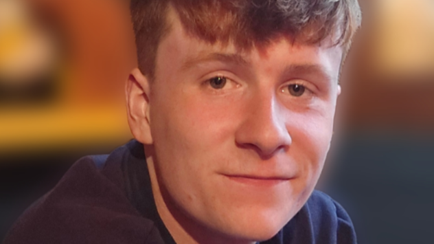 A young man, Henry Farron smiles. He has gingery hair and is wearing a navy jumper. The background in the image is blurred.