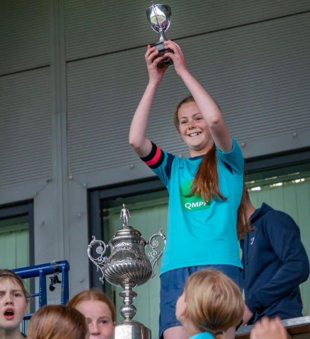 Winning girls team hold up small trophy next to larger one 