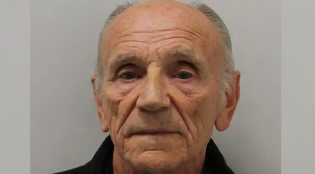 A mug shot of an elderly man who is balding. He has short, grey hair on the side of his head. 