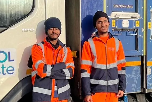 Two brothers wearing hi-vis jackets and hats stand in front of a bin lorry.