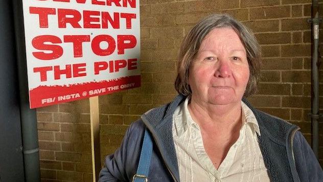 Ludlow mayor Beverley Waite wearing a light-coloured blouse and blue jacket in front of a placard reading: "Severn Trent stop the pipe"