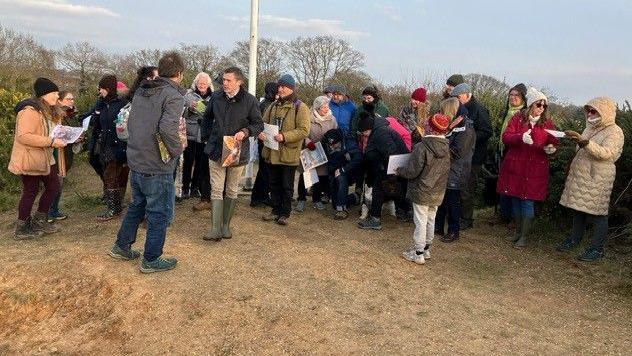 About 20 people can be seen gathering on the grassland at Middlewick Ranges, wearing coats and hats and holding posters