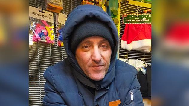 Chakib behind the counter of his shop he is wearing a dark blue coat and a dark woolen hat 