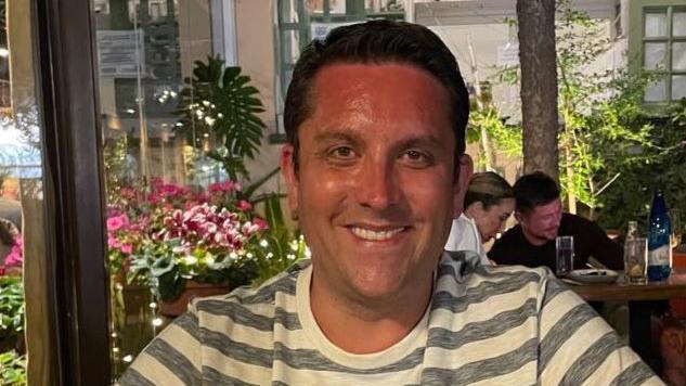 Man sat in restaurant wearing black and white striped t-shirt and smiling while looking into the camera