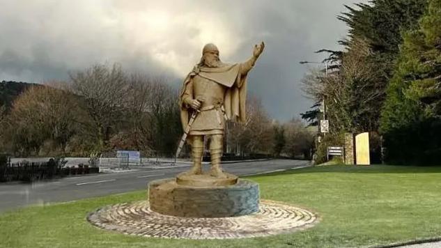 An illustration of the statue in full Viking dress with its arm stretched out. It is on a stone plinth at the edge of a grassed area next to a road with hills overlooking Peel in the background.