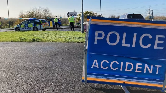 A police accident sign on the road, with police officers in the background on the scene where the fatal crash happened