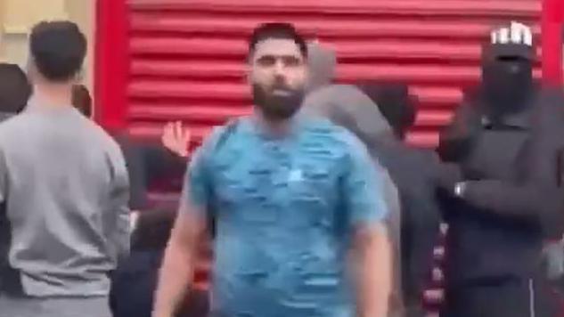 Still from CCTV footage showing a man in a blue T-shirt among a group of people with hoods up