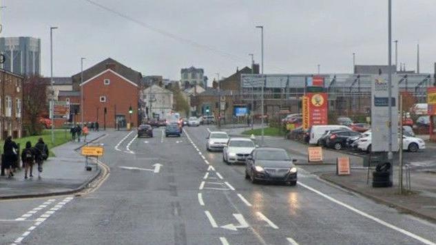 Google streetview of cars driving on King Street in Blackburn, with a garage on the right and flats on the left. People are walking on the pavement.