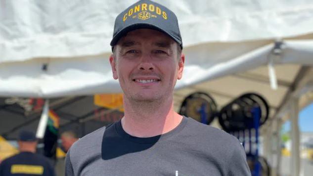 Conor Cummins smiling wearing a black T-shirt and baseball cap with the word Conrod's on it.