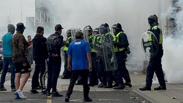 A crowd of men confront police in riot gear outside the Royal Hotel in Ferensway on 3 August during the Hull riot. Smoke billows in the background