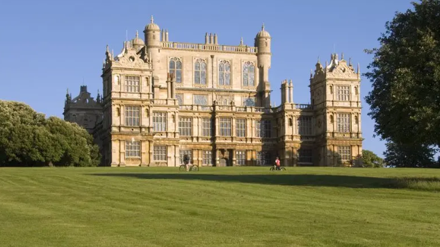 A stately home behind a large grass lawn with trees to the left and right