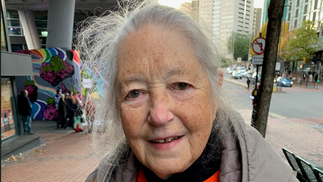 Jenny is stood on Smallbrook Queensway and has grey hair and a grey jacket on. You can see shops and shoppers in the background.