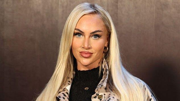 Alisha Lehmann in front of a brown background in a spotted white jacket at Paris Fashion Week