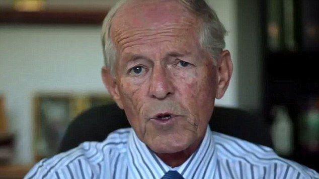 An elderly man with little hair wearing a striped smart shirt looking into the camera