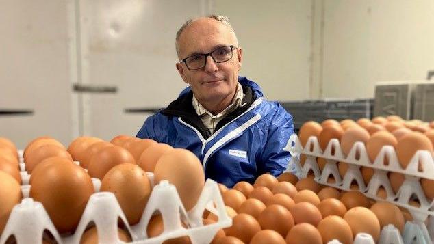 Farmer Simon Dann sits in his egg room with boxes of eggs in the foreground 