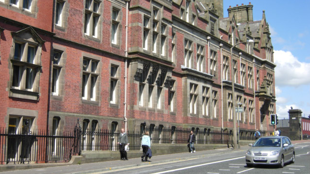 A scene shot of the red brick Preston County Hall, with pedestrians and a car moving past